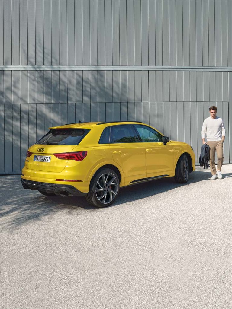 Side rear view of the RS Q3 in yellow in front of a grey wall with a man on the side